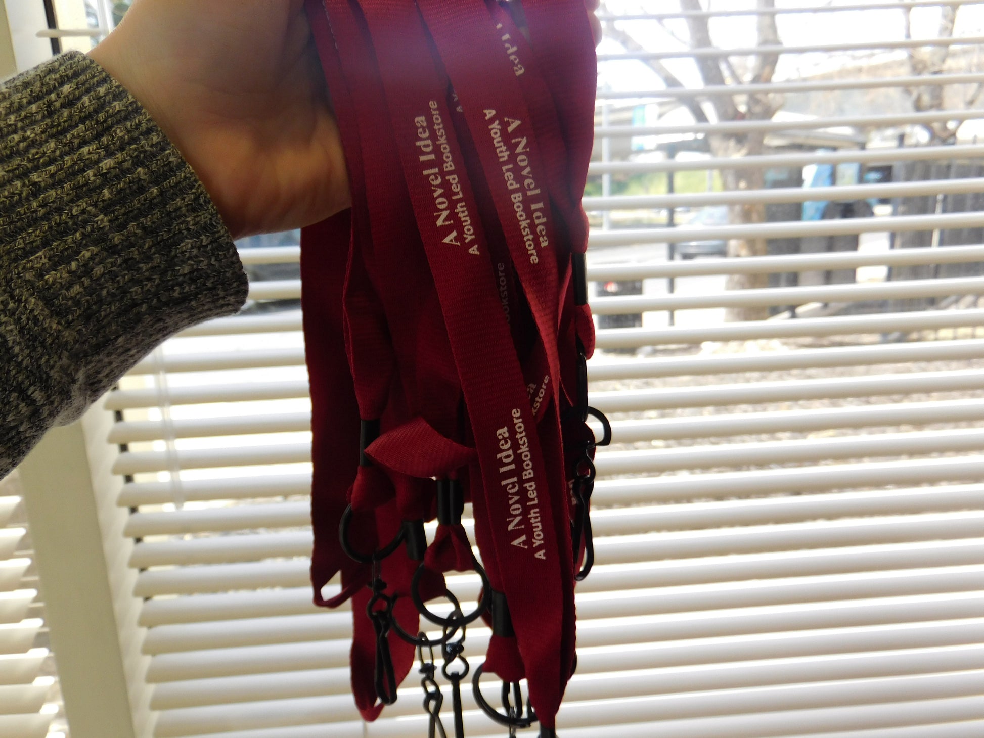 Maroon colored lanyard with white text reading "A Novel Idea. A youth Led Bookstore."